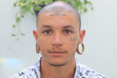 Homem jovem, de cabeça raspada, com tatuagens no rosto, usando alargador nas orelhas.
